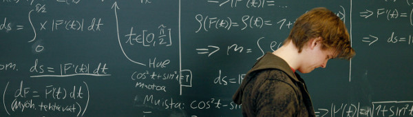 A person walking sideways in front of a blackboard with mathematical formulae written on it